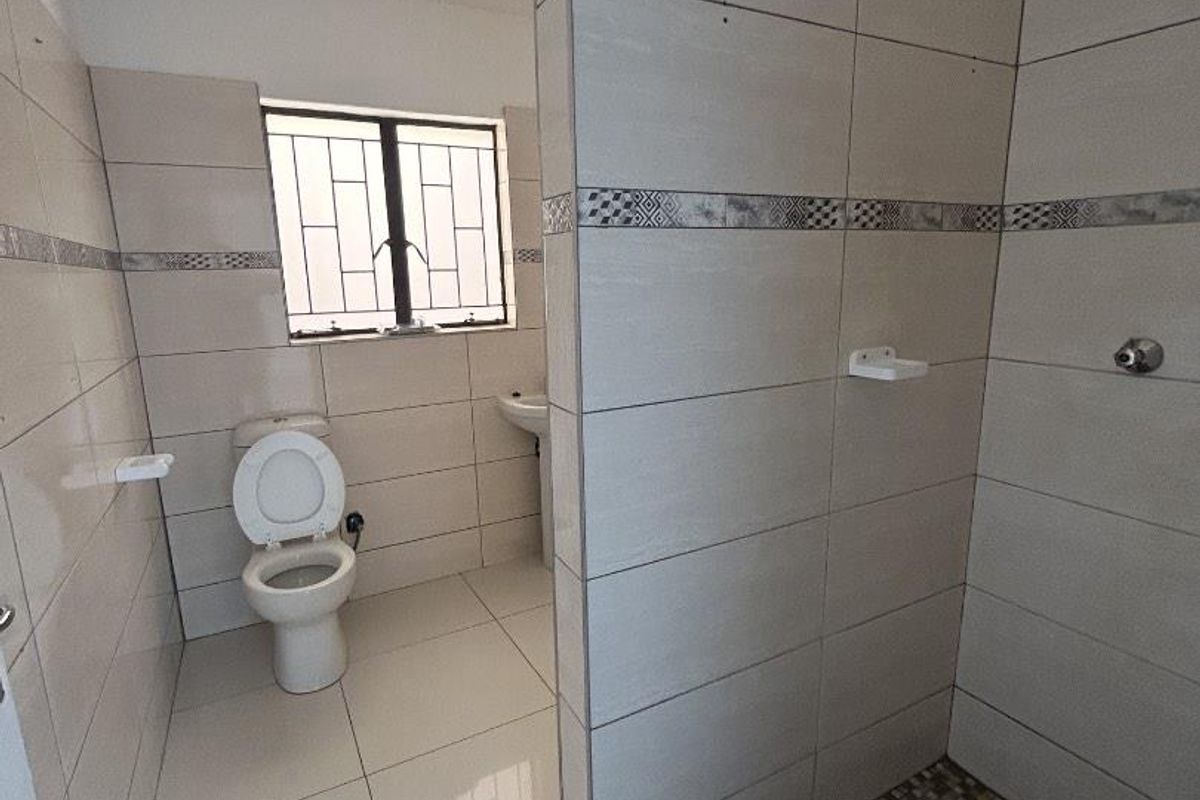 A clean, functional bathroom featuring a walk-in shower with mosaic floor tiles, a pedestal basin, and a toilet, finished with neutral wall tiling.