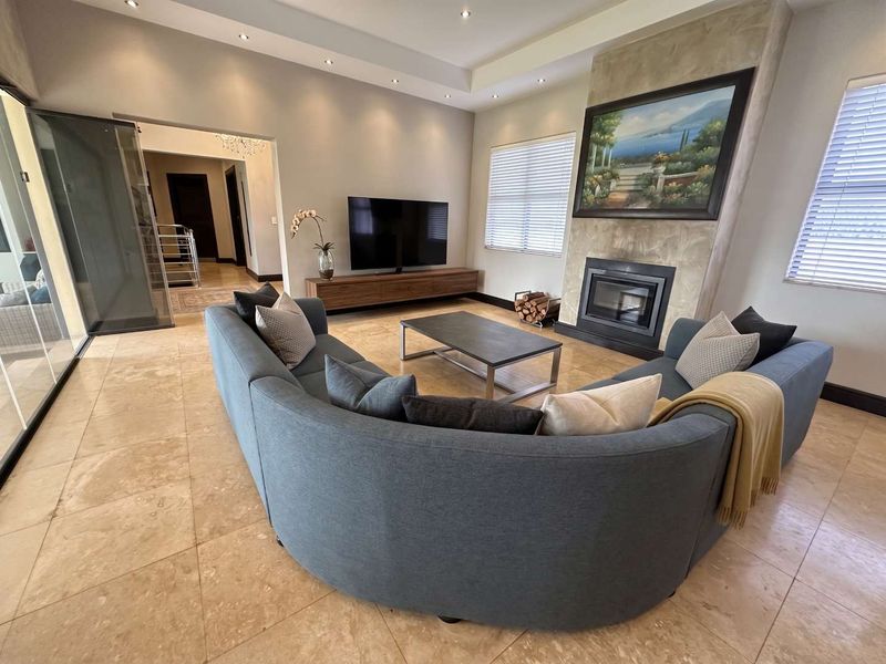 Spacious living room featuring a modern fireplace with stone surround, recessed ceiling with downlights, and neutral tiled flooring.