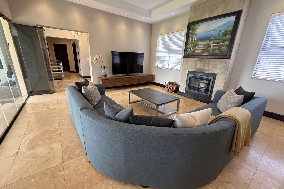 Spacious living room featuring a modern fireplace with stone surround, recessed ceiling with downlights, and neutral tiled flooring.