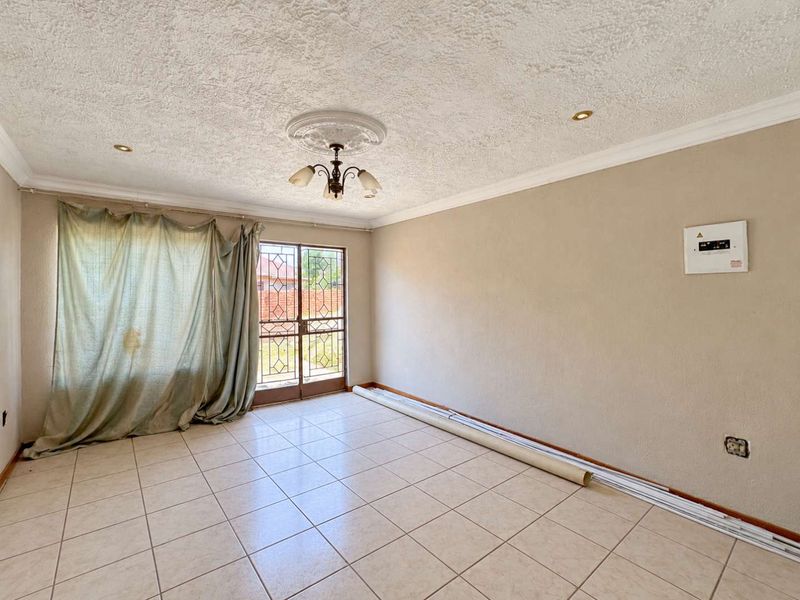 An empty living room featuring tiled flooring, a decorative ceiling rose, and a security gate leading to the exterior.