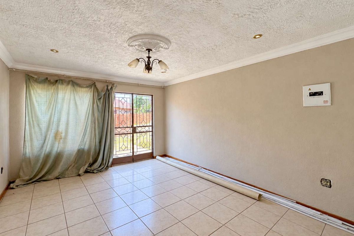 An empty living room featuring tiled flooring, a decorative ceiling rose, and a security gate leading to the exterior.