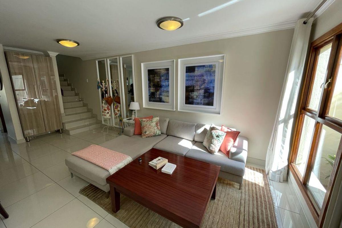 A bright living room featuring tiled flooring, a staircase, built-in cabinetry, and large wooden-framed windows allowing for natural light.