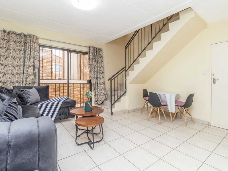 Open-plan living area featuring tiled flooring, a staircase with a metal balustrade, and a sliding glass door leading to the exterior.