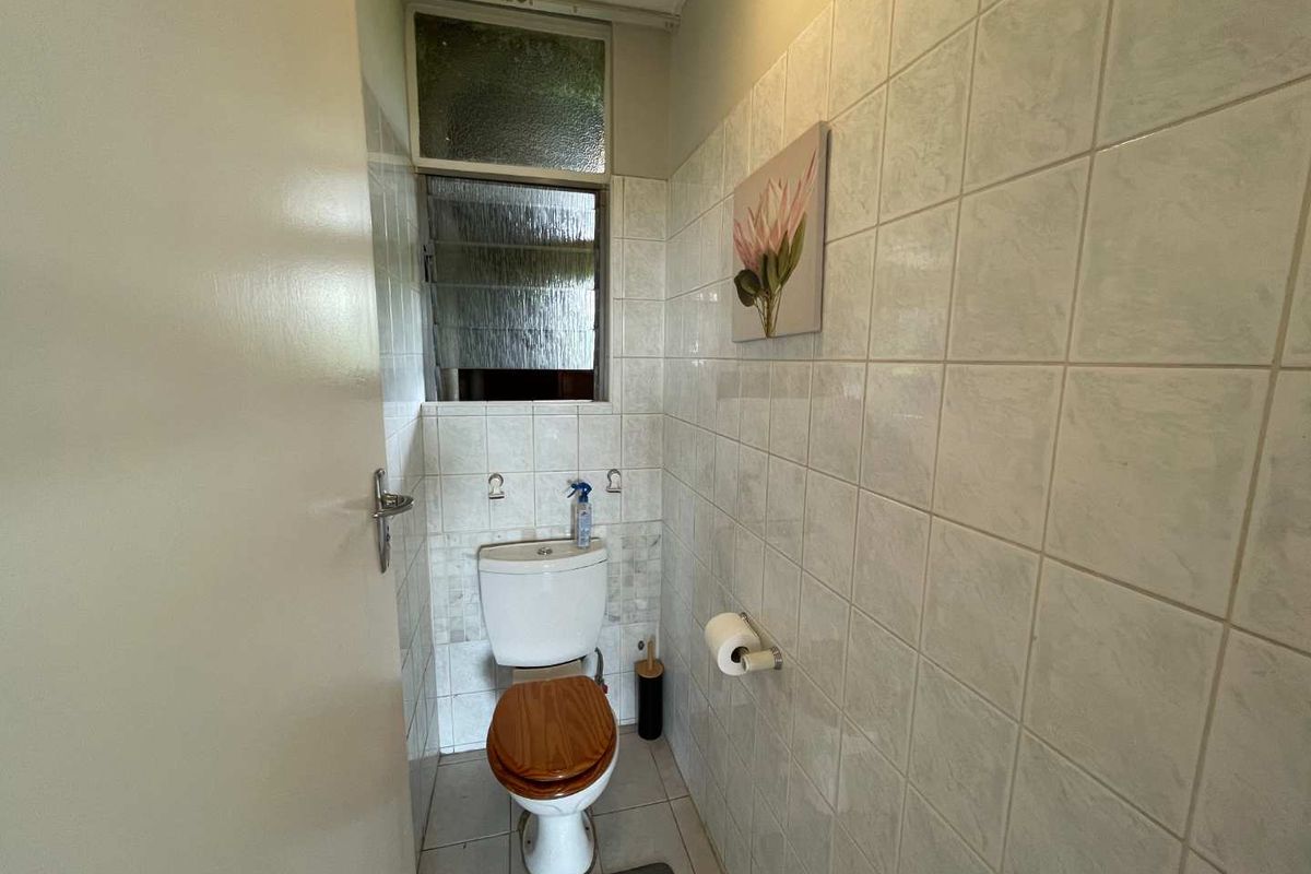A compact bathroom featuring floor-to-ceiling wall tiles, a standard toilet, and a louver window for ventilation.