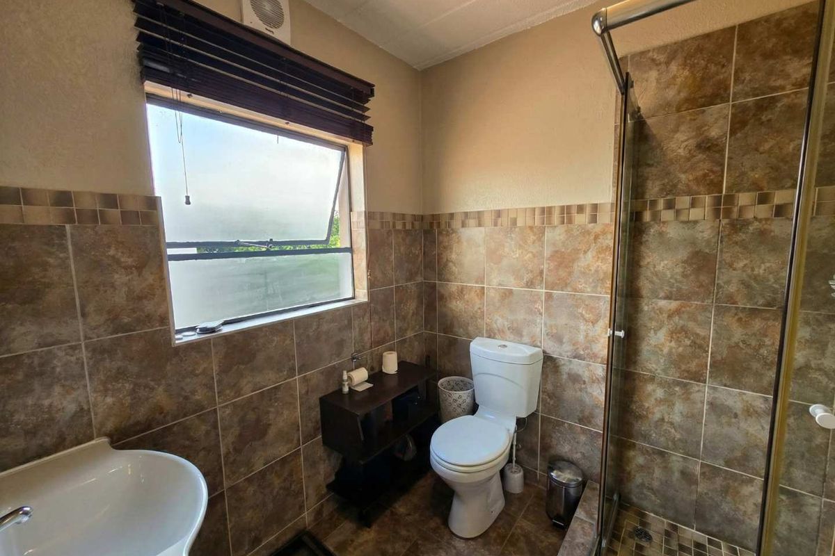 A functional bathroom featuring a shower enclosure, pedestal basin, and toilet, finished with neutral wall and floor tiling.