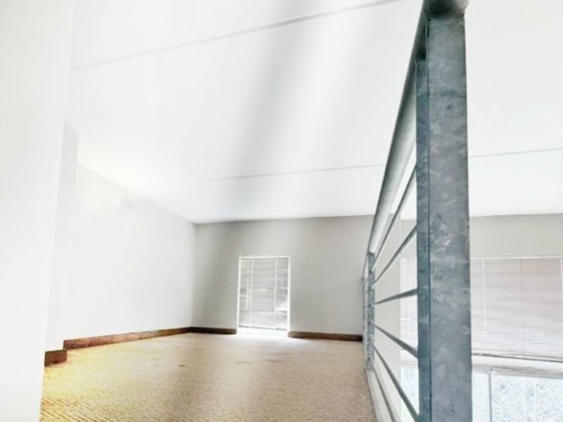 An empty mezzanine bedroom area featuring carpeted flooring and a metal safety balustrade overlooking the lower level.