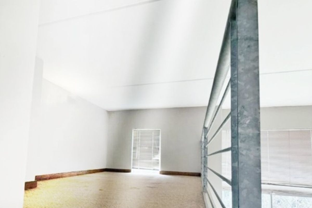 An empty mezzanine bedroom area featuring carpeted flooring and a metal safety balustrade overlooking the lower level.
