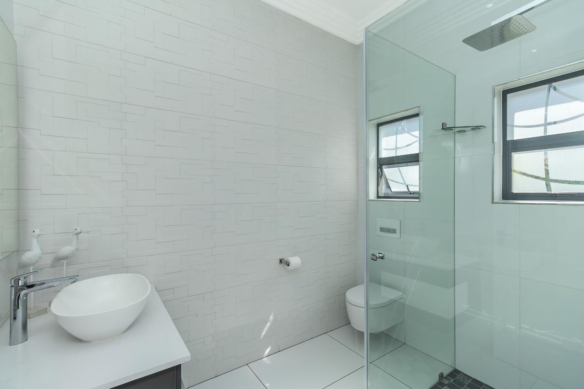 Modern bathroom featuring a sleek vessel sink, wall-mounted toilet, and a spacious glass-enclosed walk-in shower with a rainfall showerhead.
