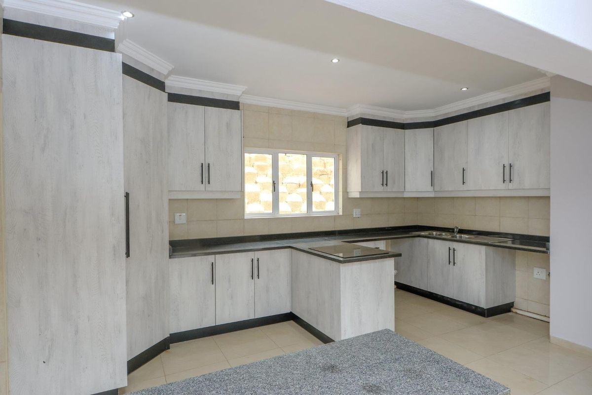 A clean, modern kitchen featuring light wood-grain cabinetry, dark stone countertops, tiled backsplash, and ample storage space in an open-plan layout.