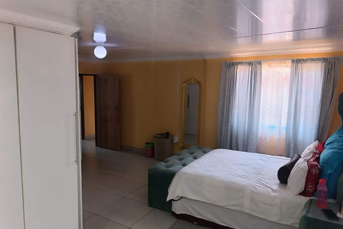 A spacious bedroom featuring tiled flooring, built-in wardrobe storage, and natural light through window curtains.