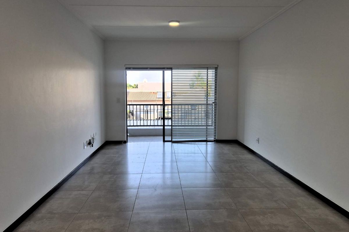 A bright, empty living room featuring neutral tiled flooring, clean white walls, and a sliding glass door leading to a balcony.