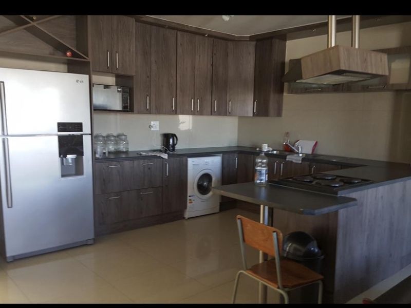 A functional kitchen featuring dark wood-look cabinetry, laminate countertops, a gas hob with extractor fan, and integrated space for a washing machine.