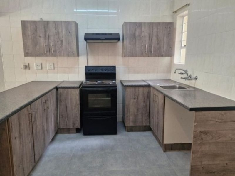 A clean, functional kitchen featuring modern wood-look cabinetry, laminate countertops, a stainless steel sink, and a freestanding stove with an extractor fan.