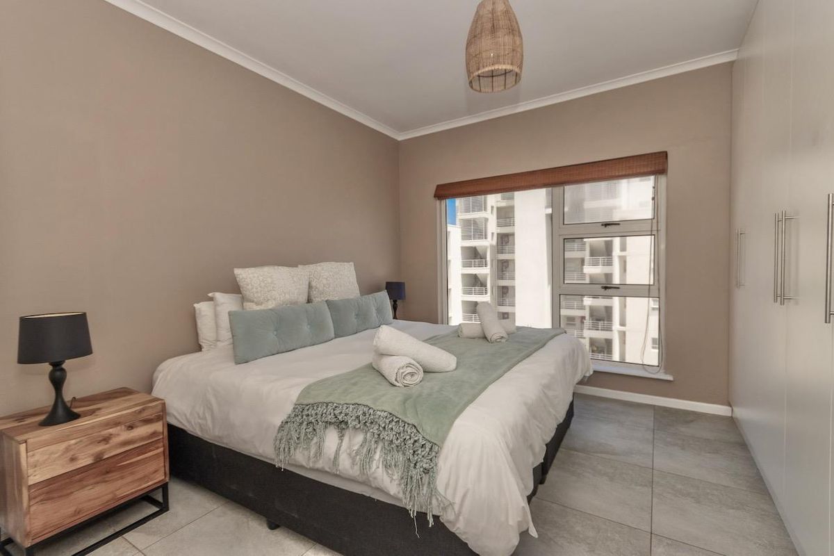A well-maintained bedroom featuring large format floor tiles, built-in wardrobes, and a window with a view of the surrounding apartment complex.
