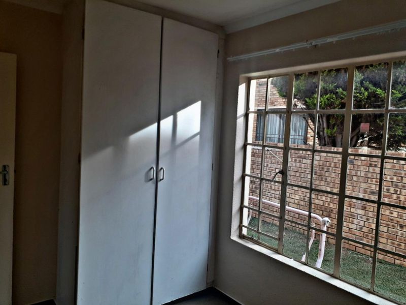 A vacant bedroom featuring a built-in wardrobe and a large steel-framed window overlooking the exterior brick wall.