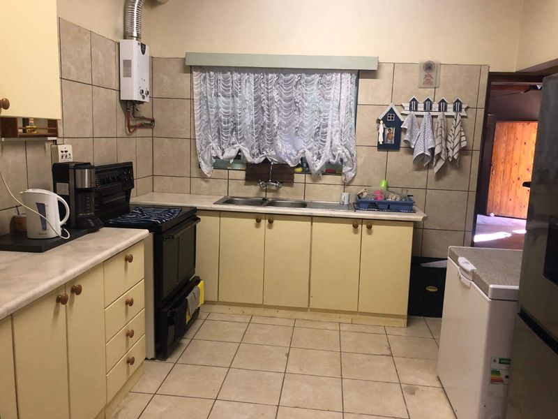 A functional kitchen featuring tiled flooring, built-in cabinetry, a double basin sink, and a gas geyser, offering a practical layout for daily use.