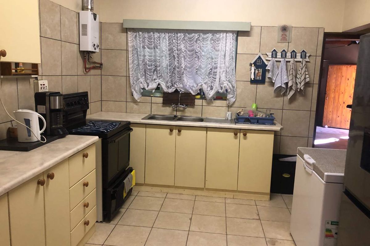 A functional kitchen featuring tiled flooring, built-in cabinetry, a double basin sink, and a gas geyser, offering a practical layout for daily use.