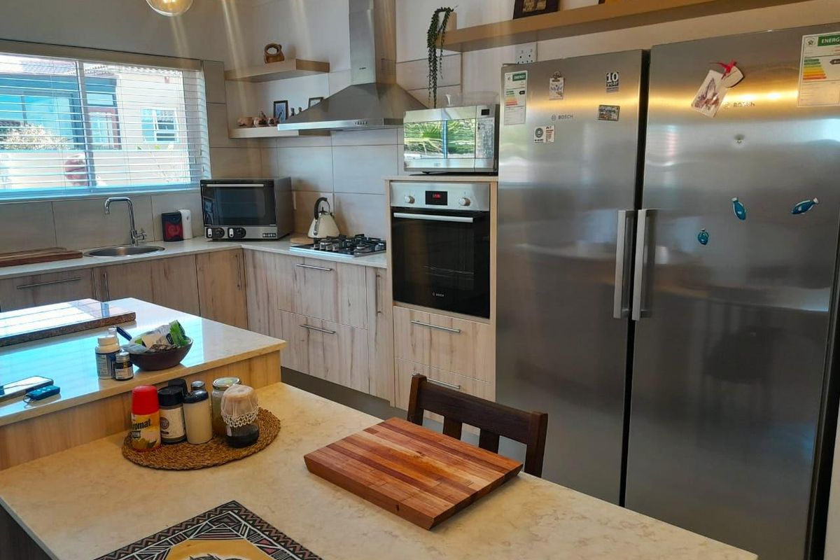 Modern kitchen featuring light wood-grain cabinetry, stone countertops, stainless steel appliances, a gas hob, and a central island with breakfast bar seating.