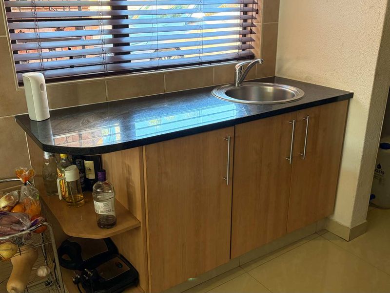 A functional scullery area featuring wooden cabinetry, a granite countertop, and a stainless steel sink with a mixer tap.