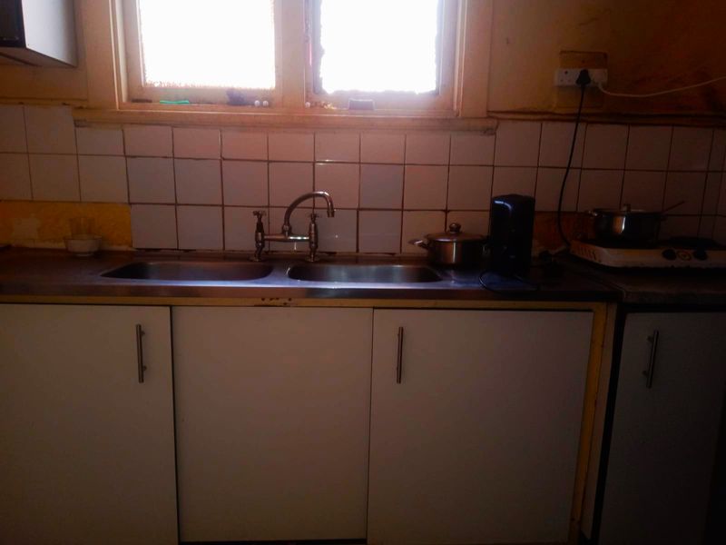 A dated kitchen area featuring a double bowl stainless steel sink, tiled splashback, and laminate cabinetry in need of renovation.