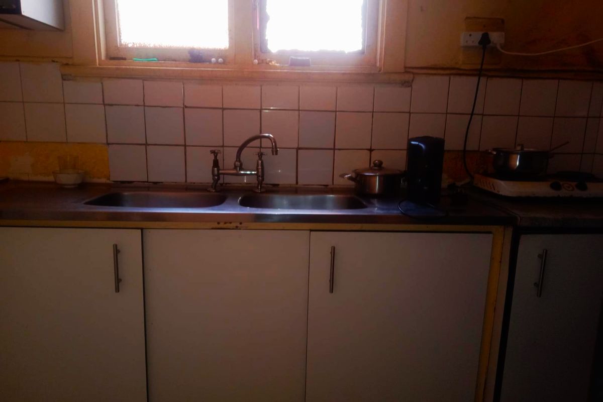 A dated kitchen area featuring a double bowl stainless steel sink, tiled splashback, and laminate cabinetry in need of renovation.