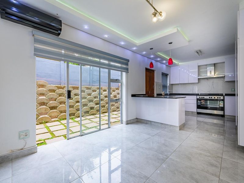 Modern open-plan kitchen and living area featuring sleek cabinetry, stone countertops, integrated appliances, recessed lighting, and direct access to a private outdoor patio.