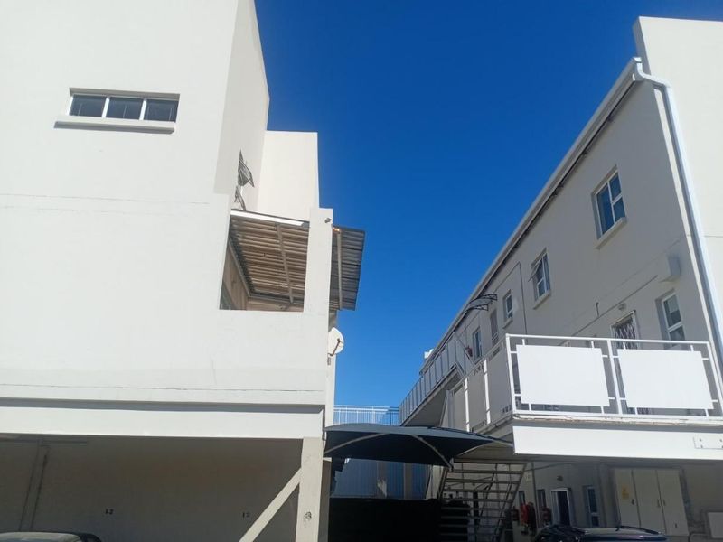 Exterior view of the apartment complex showing the rear facade, metal staircases, balcony railings, and covered parking area.