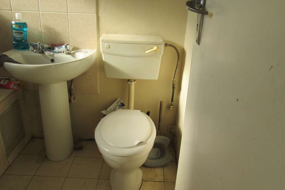 A compact bathroom featuring a pedestal basin and standard toilet, requiring cosmetic updates and maintenance to improve the overall condition of the space.