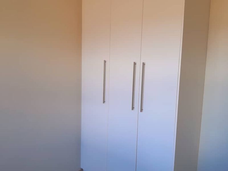 A clean, empty bedroom featuring neutral tiled flooring and a modern, white built-in wardrobe with sleek metal handles.