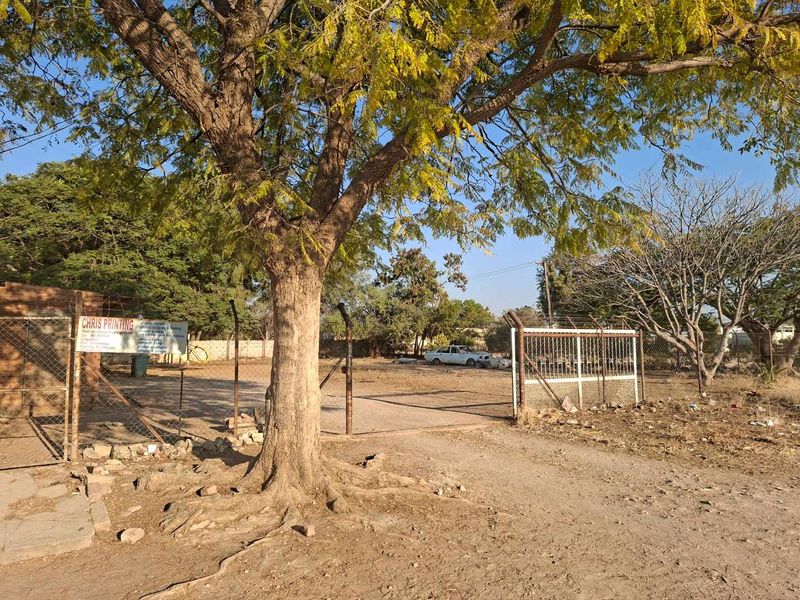 An exterior view of a property entrance featuring a chain-link fence, metal gate, and paved driveway area.