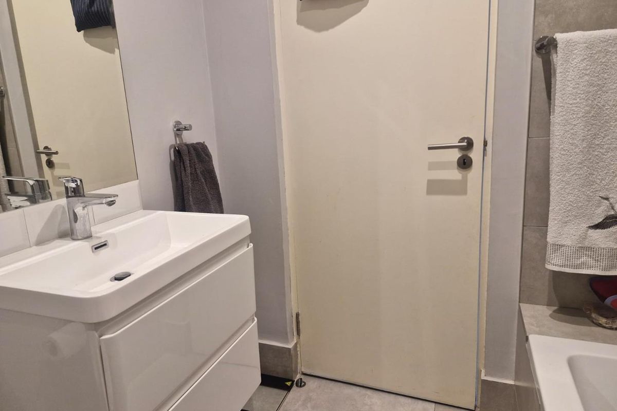 A modern bathroom featuring a white vanity with a basin, a bathtub, and neutral floor tiling.