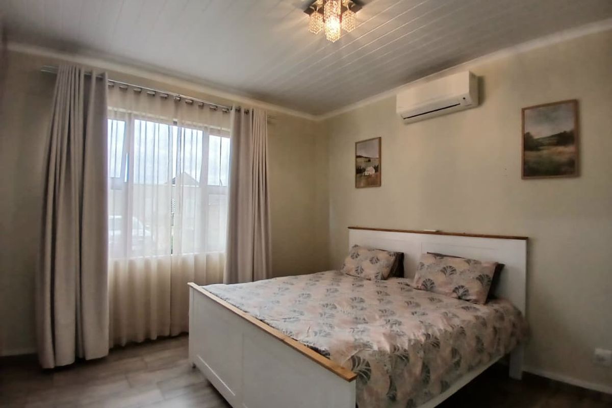 A well-maintained bedroom featuring timber-look flooring, a tongue and groove ceiling, a crystal chandelier, and a wall-mounted air conditioning unit.