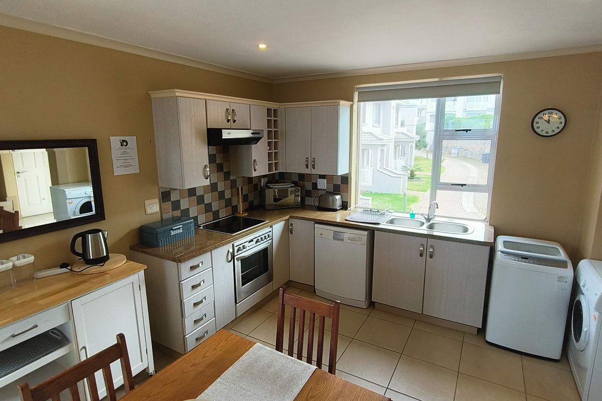 Functional kitchen featuring light wood-finish cabinetry, granite countertops, tiled backsplash, and integrated appliances, with a window overlooking the complex grounds.