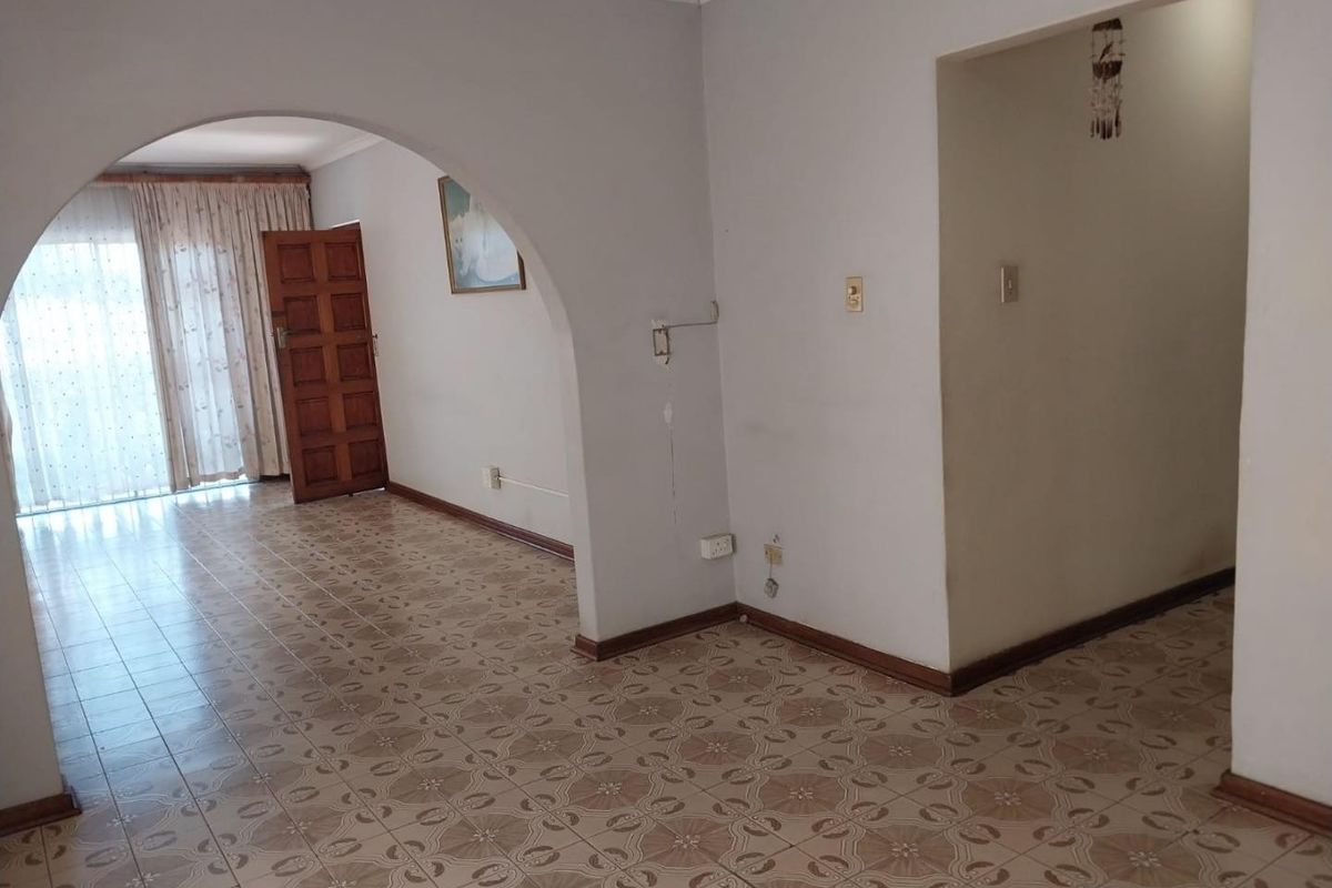 An empty living area featuring tiled flooring and a distinctive architectural archway, providing a blank canvas for renovation and interior design updates.