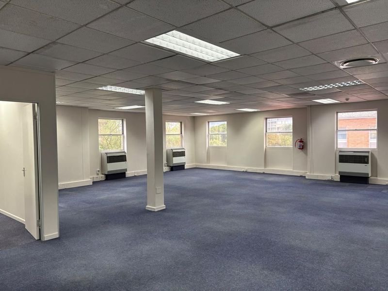 Spacious open-plan office area featuring a suspended ceiling, recessed lighting, carpeted flooring, and multiple wall-mounted air conditioning units.