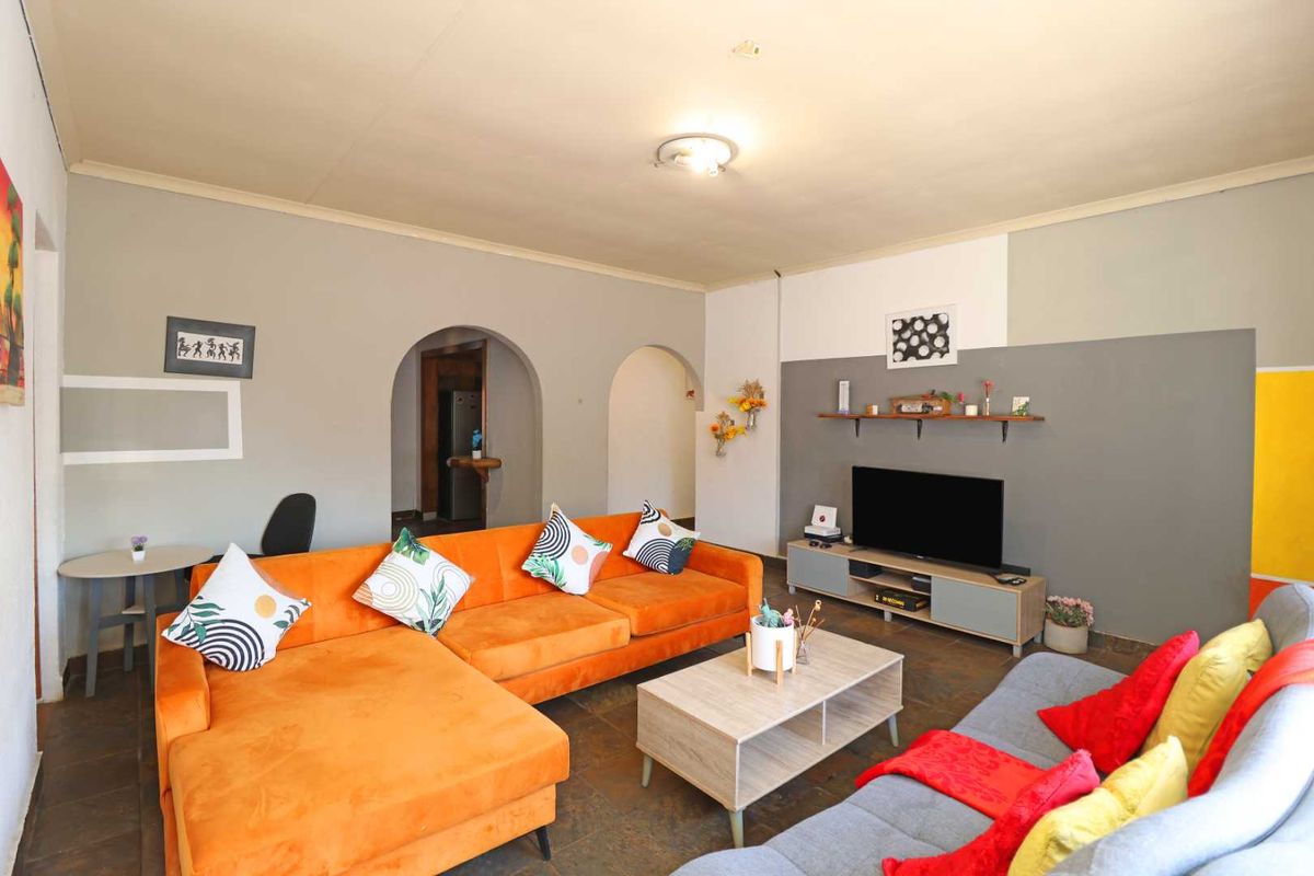 A spacious living room featuring tiled flooring, distinctive arched doorways leading to adjacent areas, and neutral wall finishes with decorative accent painting.