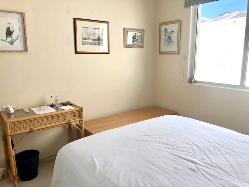 A functional bedroom featuring neutral walls, carpeted flooring, and a window with a roller blind, providing a bright and comfortable living space.