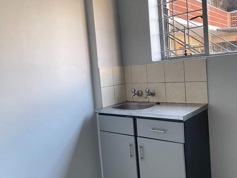 A compact kitchen area featuring a single stainless steel sink, built-in base cabinetry, tiled backsplash, and security bars on the window.
