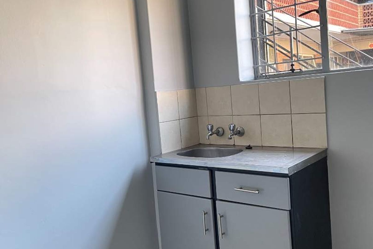 A compact kitchen area featuring a single stainless steel sink, built-in base cabinetry, tiled backsplash, and security bars on the window.