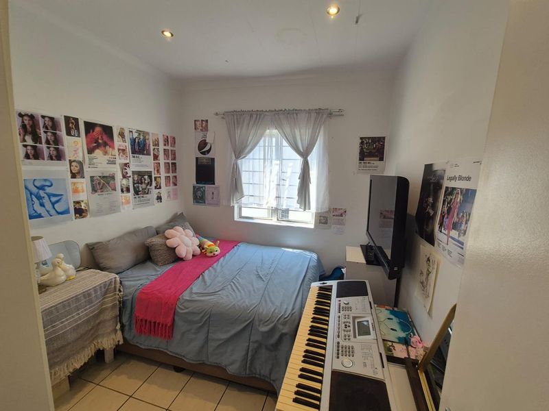 A compact bedroom featuring tiled flooring, recessed downlighting, and a window fitted with security bars.