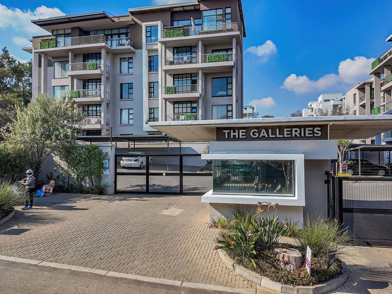 Front entrance view of The Galleries apartment complex, featuring a secure gated access point, guard house, and modern multi-story residential building.