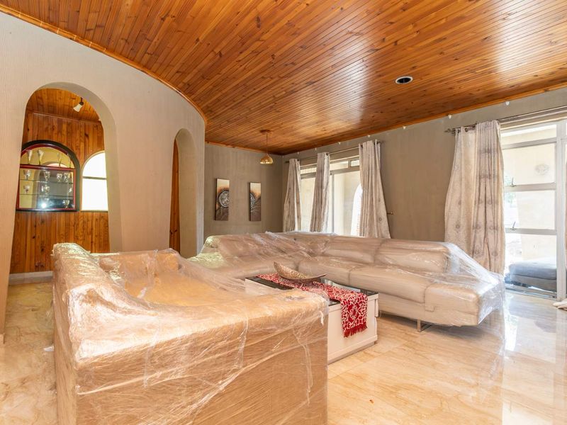 Spacious living room featuring a distinctive timber tongue and groove ceiling, arched architectural details, and polished tile flooring with access to the patio.