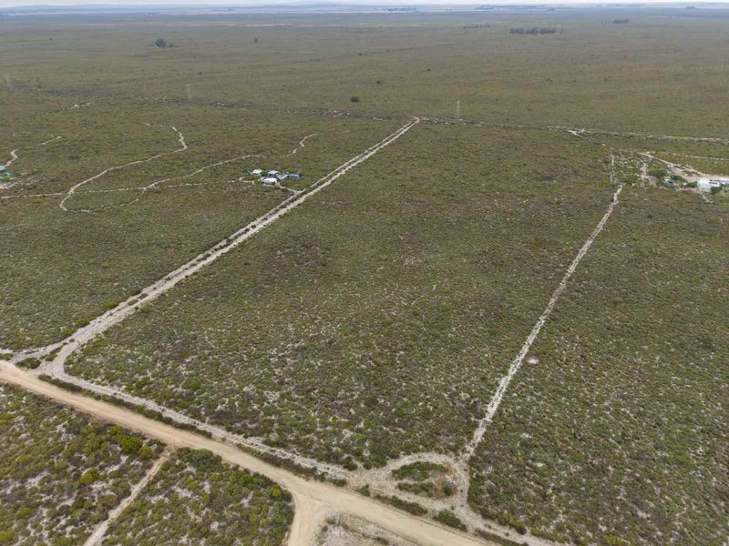 Aerial view of a large, flat agricultural land parcel featuring natural vegetation, dirt access roads, and fenced boundaries.