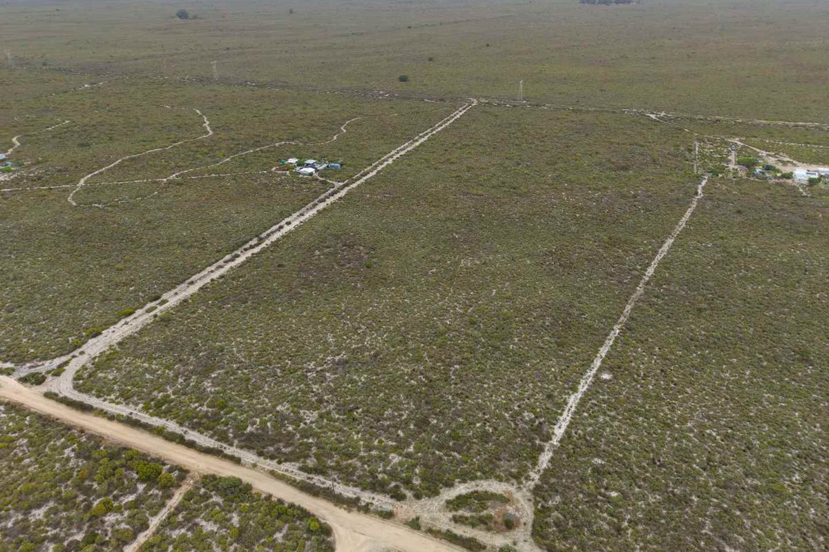 Aerial view of a large, flat agricultural land parcel featuring natural vegetation, dirt access roads, and fenced boundaries.