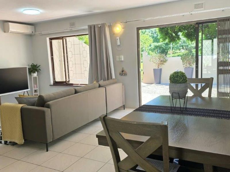 Bright open-plan living and dining area featuring tiled floors, modern slatted wood wall accents, and large sliding doors leading to an outdoor space.