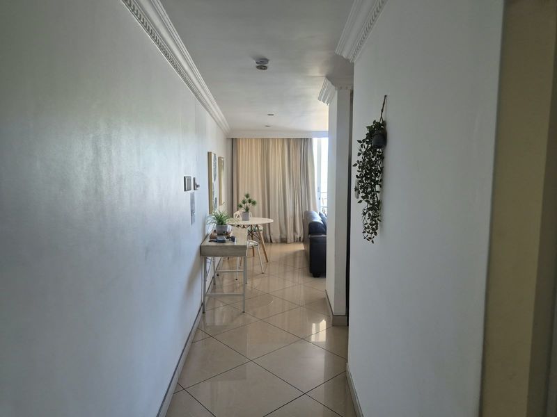 A bright hallway featuring polished tiled flooring and decorative crown molding, leading towards an open-plan living area with natural light.