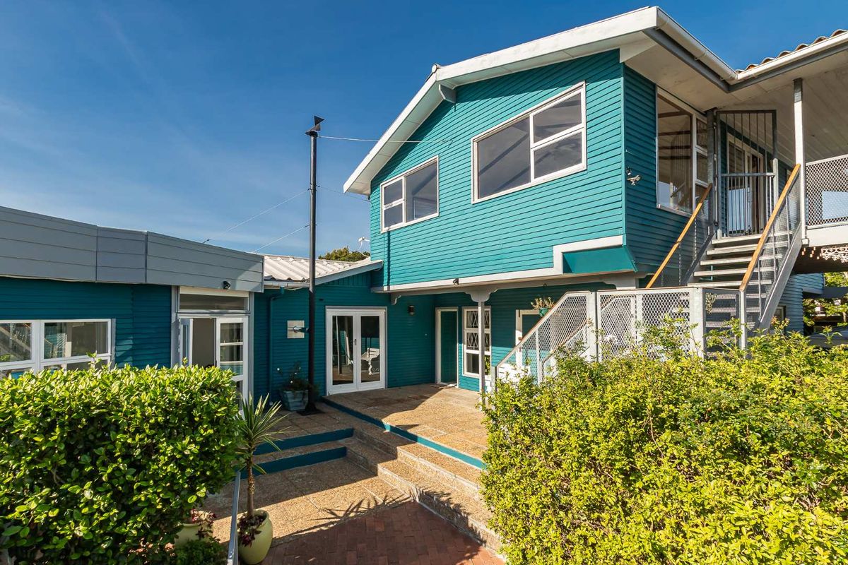 Rear exterior view of a two-story house featuring blue weatherboard cladding, a paved patio area, and an external staircase leading to the upper level.
