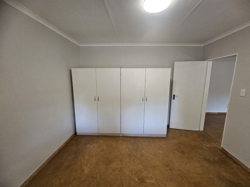 A simple, empty bedroom featuring built-in white cupboards, neutral walls, and exposed flooring, offering a blank canvas for personalization.