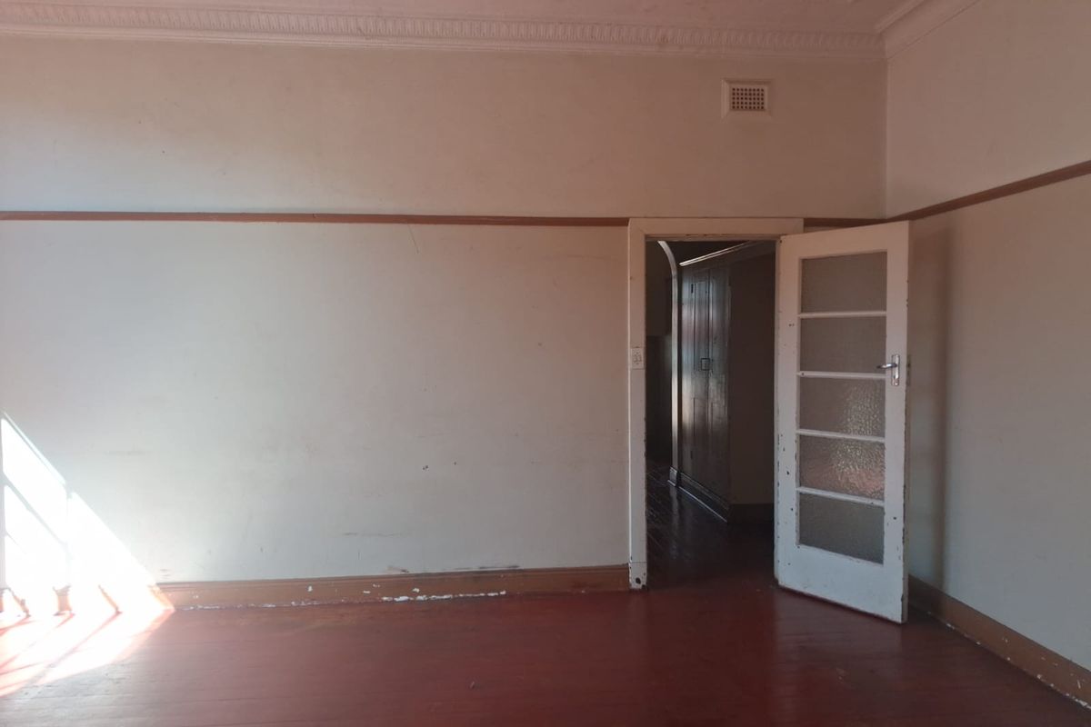 An empty bedroom featuring original timber flooring, decorative ceiling detailing, and a classic glass-panelled door, offering a blank canvas for renovation.