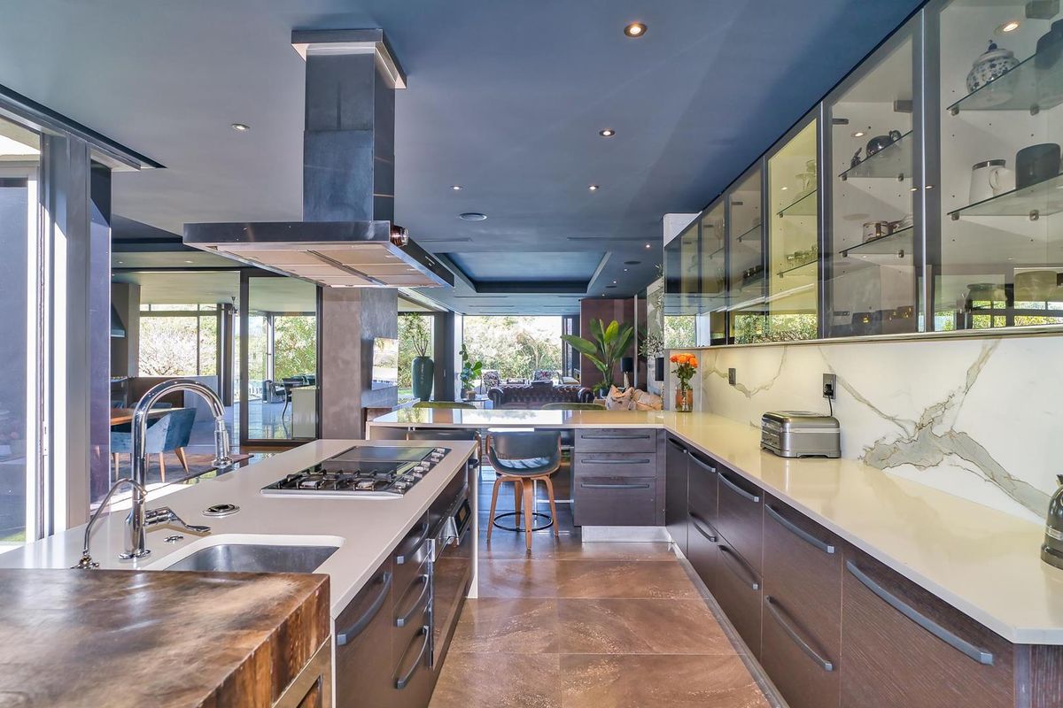 Modern open-plan kitchen featuring a large island with gas cooktop, stone countertops, sleek cabinetry, and seamless flow to the outdoor living area.